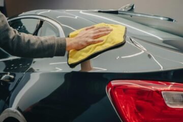 Close-up of hand polishing a shiny car with a yellow cloth indoors.