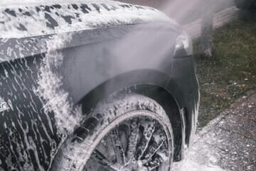 Close-up of a luxury car wheel being thoroughly washed with foam outdoors.