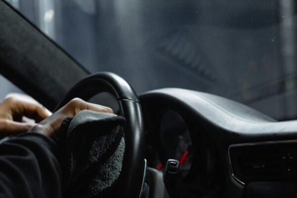 Close-up of a person cleaning a car's dashboard and steering wheel, focused on interior maintenance.