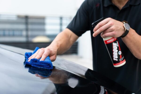 Hands cleaning car with microfiber cloth and spray cleaner for a shiny finish.